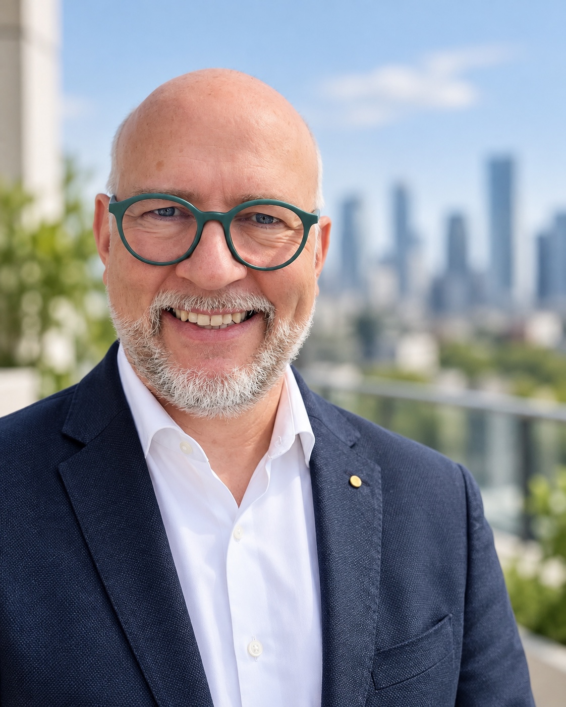 Klaus Pfeiffer wearing green glasses and a navy jacket, with a city skyline in the background